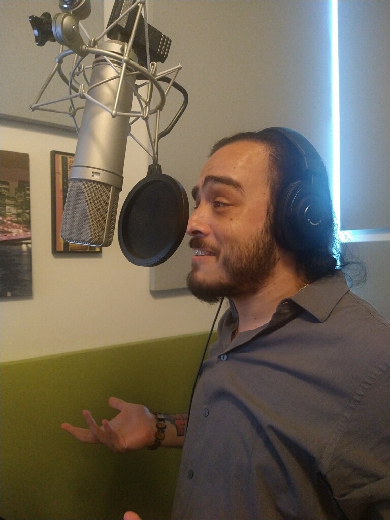 A voiceover artist recording in a studio, speaking into a microphone while wearing headphones, with an expressive hand gesture.